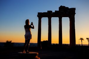 Silhouette of girl photographing on phone Temple of Apollo at sunset