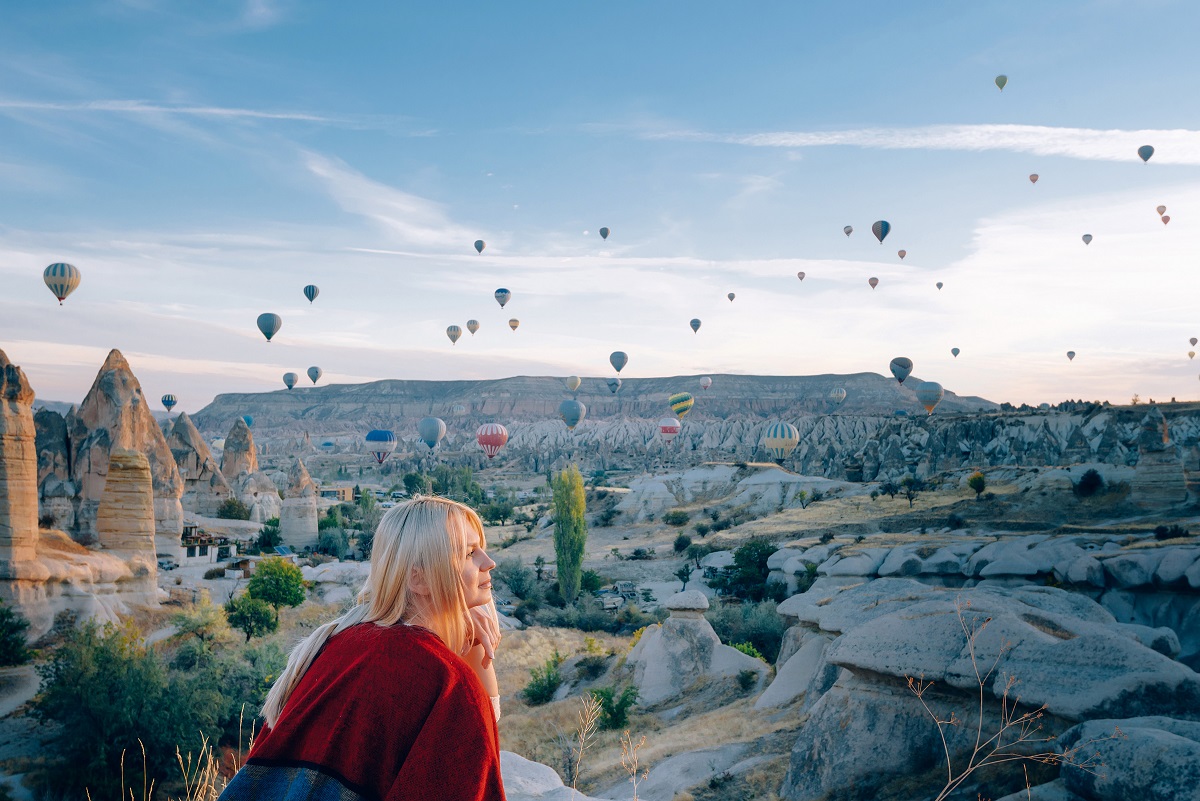 girl in ethnic clothes at dawn watching the flight a lot of balloons fly over the valley of love